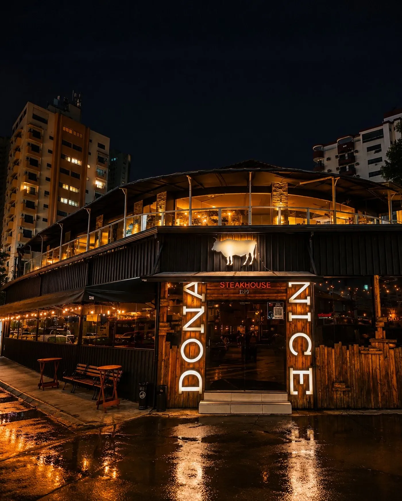 Fachada da Dona Nice à noite, com o touro iluminado e as letras DONA NICE em madeira